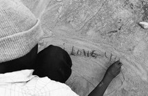 man writing I LOVE YOU in sand