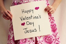A Little girl holding up a sign that read's Happy Valentine's Day Jesus