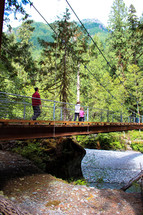 people crossing over a swinging bridge 