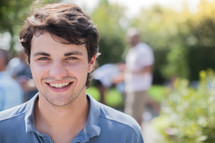 headshot of a young man and friends talking at a backyard summer party