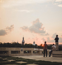 Men on a roof looking at a skyline of mosques and domes at sunset.