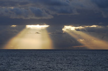Sun light shining through dark clouds over the ocean. Sunrays radiating from behind storm clouds.