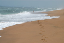 Foot steps in the sand on a beach with waves