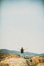 Man standing with open arms on a rocky hill.