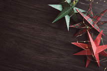 Paper Christmas stars and mini lights on a dark wood background with copy space