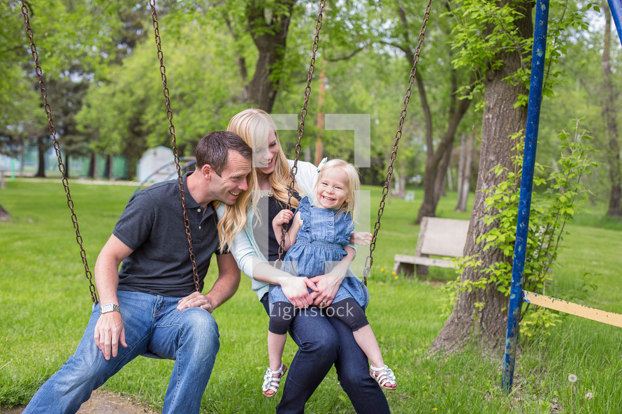 a father and mother on a swing set with their daughter 