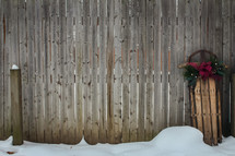 sled decorated for Christmas leaning against a wood fence 