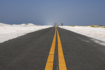 Open road through white sand dunes with double yellow lines