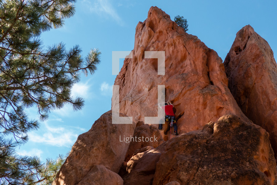 rock climber on side of rugged rock with pleasant lighting, evergreen, and blue sky