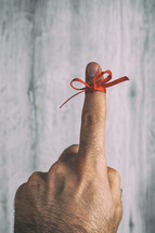 Man is showing his finger with a red ribbon tied around it, serving as a visual reminder