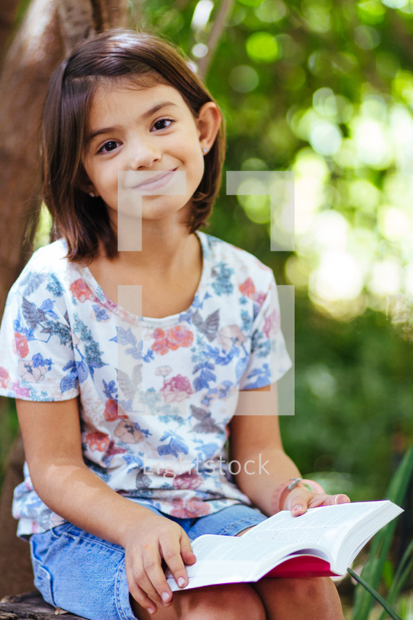girl child reading a Bible outdoors 