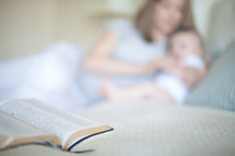 Mother and infant daughter laying on the bed with an open Bible.
