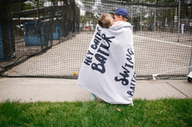 kids wrapped in a blanket at a batting cage 