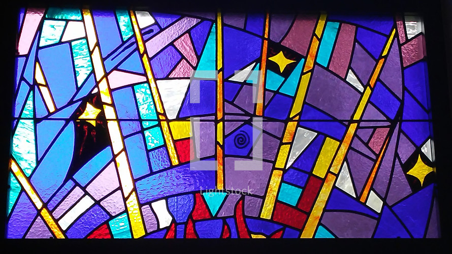 A colorful stained glass window with blue, lavender, purple, red and gold and symbols adorn a church worship center in a prayer chapel. 