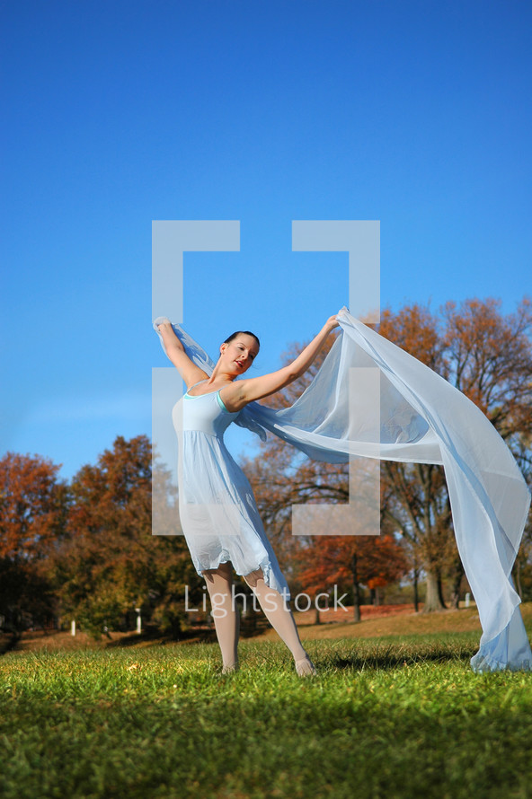 woman dancer, in a green field, autumn trees in the background