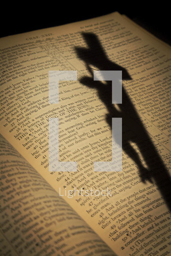 shadow of a crucifix on the pages of a Bible opened to the passion account