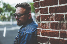 man in sunglasses leaning against a brick wall 