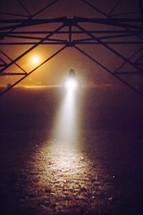 A man shining a flashlight on the ground in the fog 