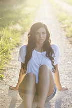 woman sitting on a dirt road under the glow of sunlight 