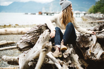 a woman sitting on a pile of driftwood on a beach 