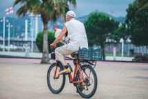 An old man rides a bicycle with a rooster