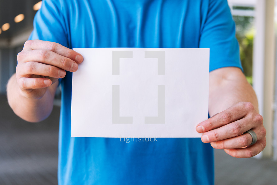 Close up of a man holding up a blank flyer against his torso.