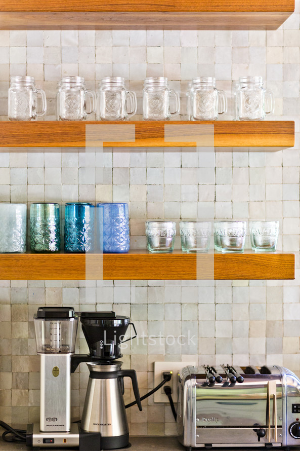 Kitchen wood shelf with appliances blender, coffee maker, toaster, mason jars, cups, glasses, tile back splash