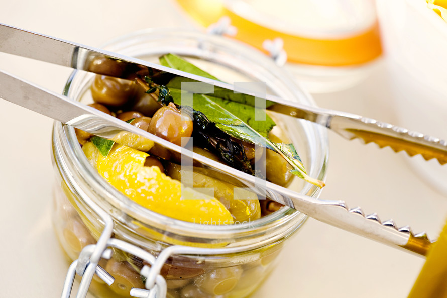 Jar of olives peaches bay leaves tongs 