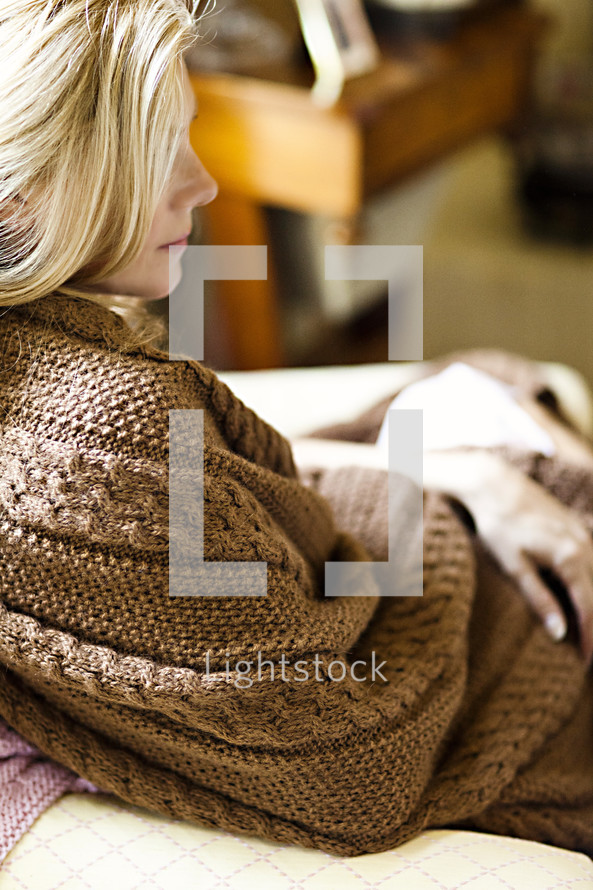 A sitting woman wrapped in a brown blanket.