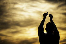 silhouette of a man holding up communion bread and wine to the sky in worship and praise to the Lord