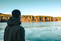 a man in jacket standing on the shore of a frosty lake 
