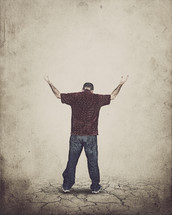 man standing on parched soil with his hands raised in worship to God