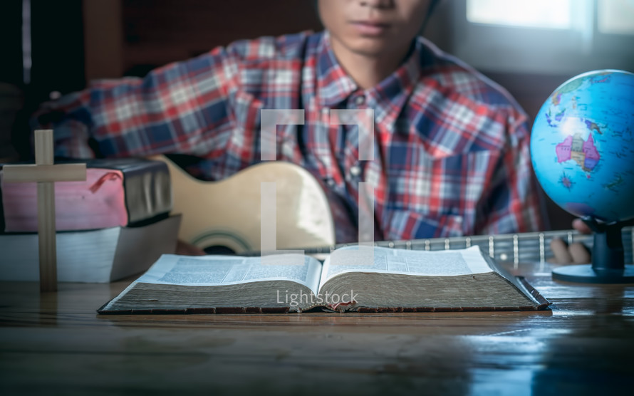 a young man playing a guitar in front of an open Bible 
