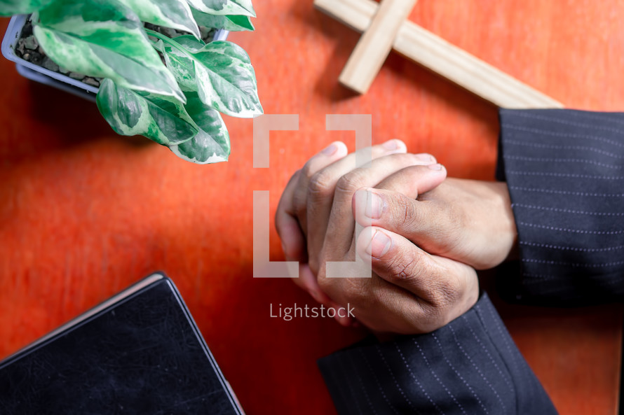 Close up hands praying on wooden table, view from above