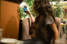 Girl sitting in a cafe taking a picture with her cell phone.