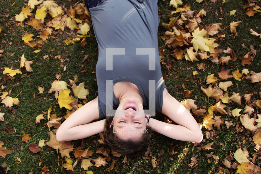 a young woman lying in grass surrounded by fall leaves 