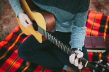 man with a guitar on a plaid blanket 
