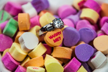 A diamond engagement ring among colorful heart shaped candies.