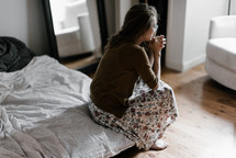 a woman sitting at the edge of a bed praying 