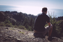Contemplating man sitting on a hill overlooking nature.
