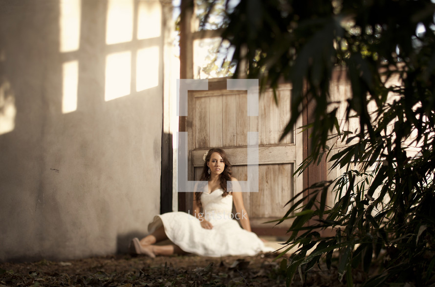 bride sitting on the ground outdoors in front of a door 