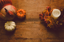 Turkey figurine, miniature pumpkins, and a candle with a wreath of fall leaves on a wooden table -- Thanksgiving decor.