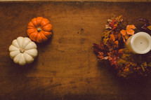 Miniature pumpkins and a candle with a wreath of fall leaves on a wooden table -- Thanksgiving decor.