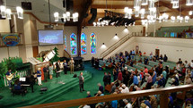 A Pastor leads his congregation in prayer during a traditional worship service surrounded by stained glass windows, a worship band and musicians during a Sunday morning time of worship and praise. 