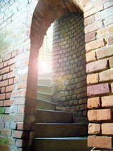 sunlight shining into a spiral staircase and winding stair well  in a brick passage way 