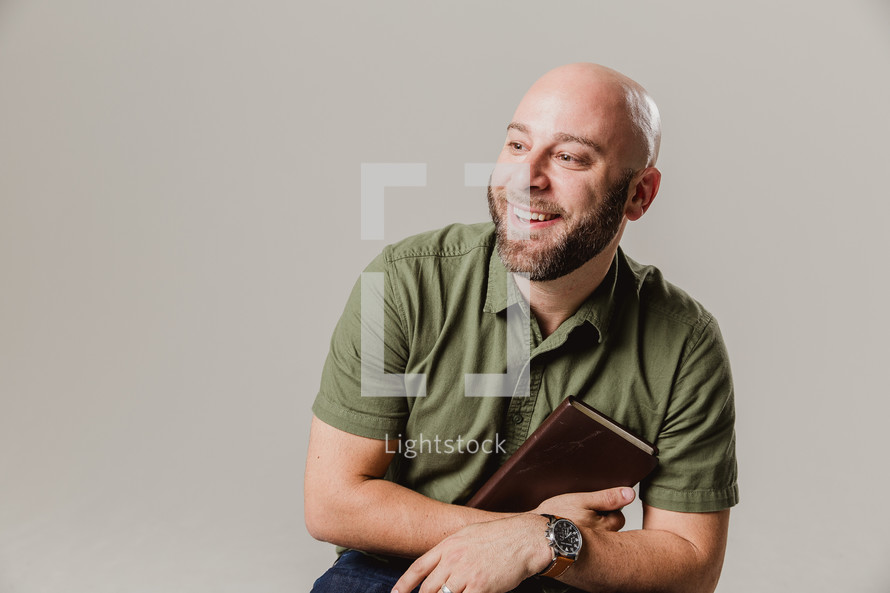 man sitting on a stool holding  a Bible 