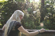 teen girl with long blonde hair looking over a railing into a forest 