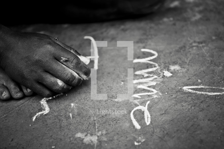 A child writes on the ground using chalk