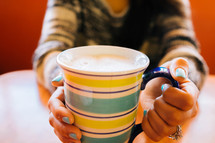A women holding a striped mug filled with a frothy beverage.