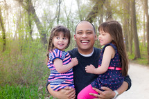 Smiling father standing outside holding his daughters.